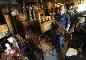 George Cushing, co-owner of Cushing Clutter Antiques in Plainfield, examines one of about 600 chairs in his inventory on Wednesday.